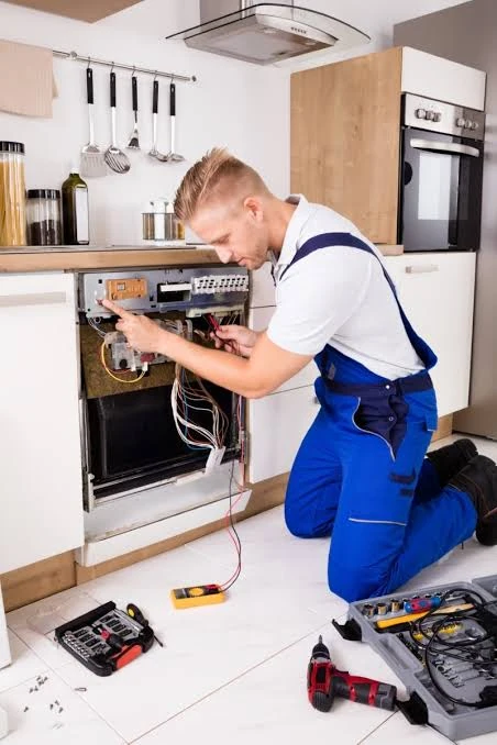 Technician using electrical test leads on an exposed built-in appliance panel
