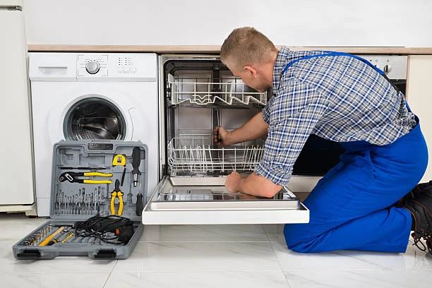 Technician inspecting an open dishwasher beside a washing machine