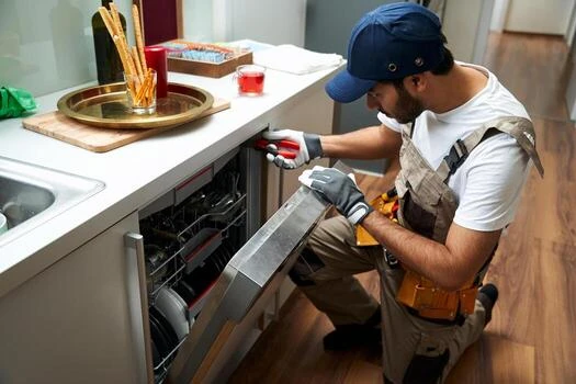 Technician wearing gloves repairing a dishwasher with a screwdriver