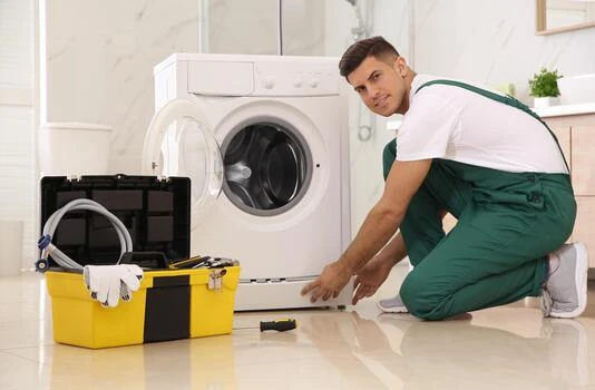 Technician repairing the lower front of a washing machine beside a yellow toolbox