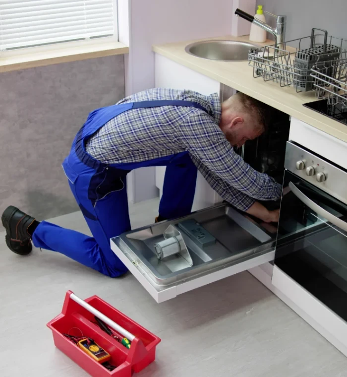 Technician in blue overalls inspecting an open under-counter dishwasher
