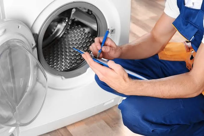 Technician recording inspection notes beside an open front-loading washing machine